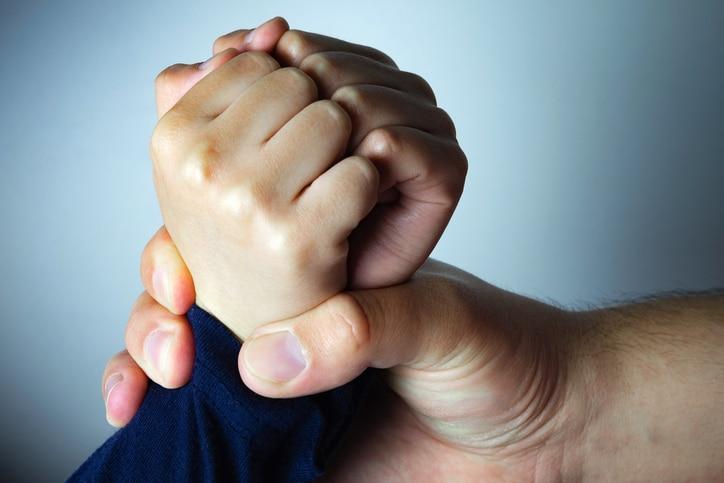 Father roughly holds the hands of his son.
