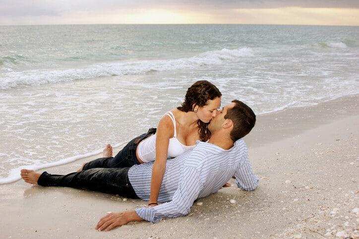 young adult couple kissing at the beach as the sun sets.