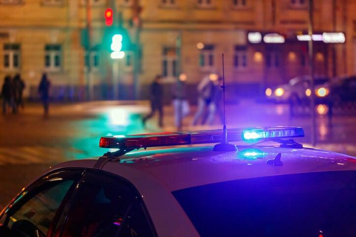 night police car lights in city street with blurry pedestrians crossing road in the background.