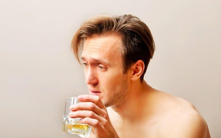 Drunk man sitting on bed and drinking whiskey.