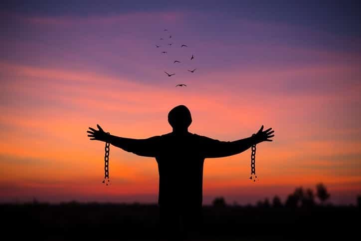 Silhouette of young man standing alone with beautiful sky at sunset open both arms with chains on his arms. He felt free from the shackles tied to his arms.