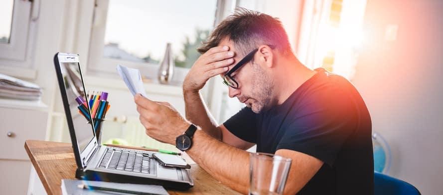 Man sitting in home office, reading letter and felling worried. With one hand holding letter and with other hes forehead